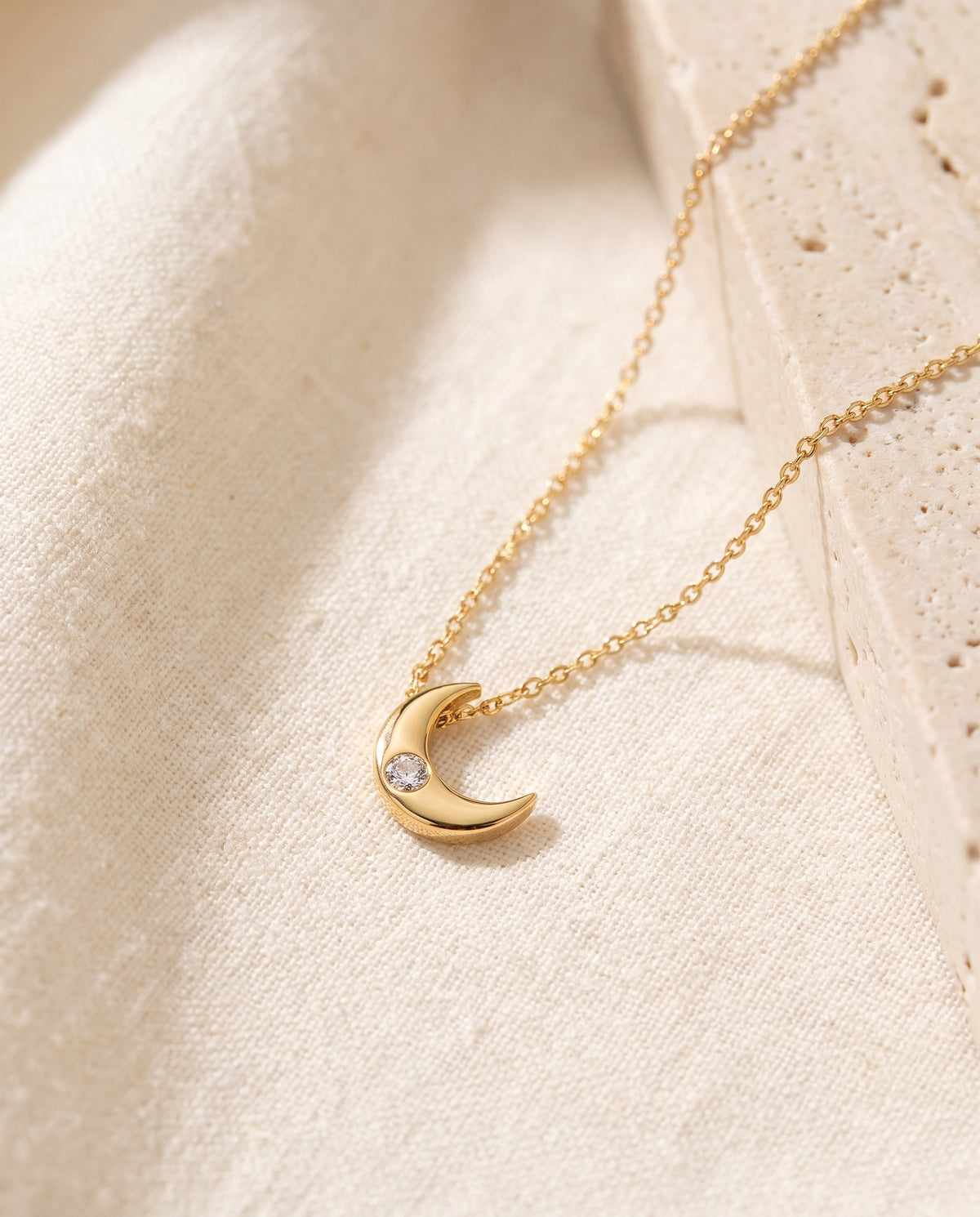 Crescent Moon Pendant Necklace with a single cubic zirconia on a fine gold-plated chain on ivory linen