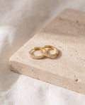 Pair of gold-plated Huggie Hoop Earrings set with a row of cubic zirconia on a travertine block