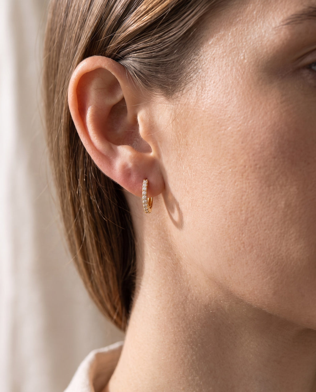 Woman wearing the Cubic Zirconia Huggie Hoop Earrings close to the earlobe