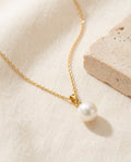Glass Pearl Drop Necklace with a single white glass pearl on a fine gold-plated chain on ivory linen