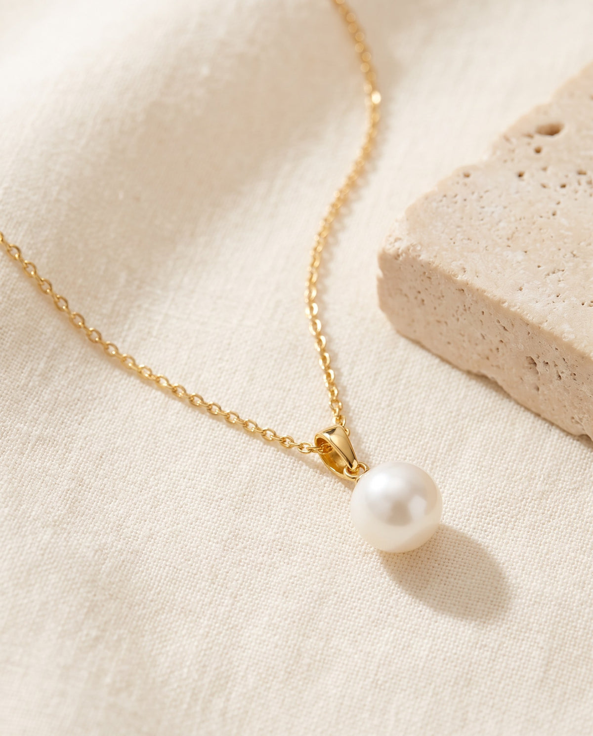 Glass Pearl Drop Necklace with a single white glass pearl on a fine gold-plated chain on ivory linen