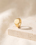 Oval Signet Ring in 18k gold-plated stainless steel with a plain polished face on a travertine block