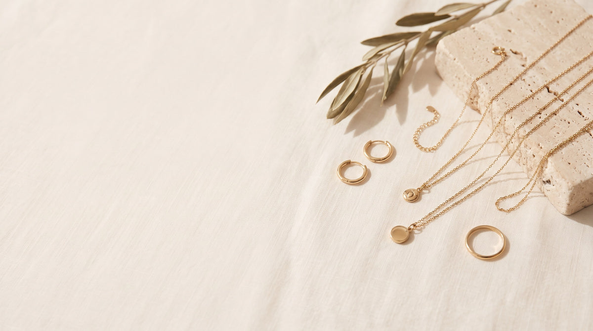 Gold-plated necklaces, hoop earrings and a ring arranged on ivory linen beside a travertine block