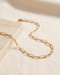 Paperclip Chain Necklace in 18k gold-plated stainless steel on ivory linen beside a travertine block