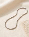 Silver-tone Snake Chain Necklace in polished stainless steel on ivory linen beside a travertine block