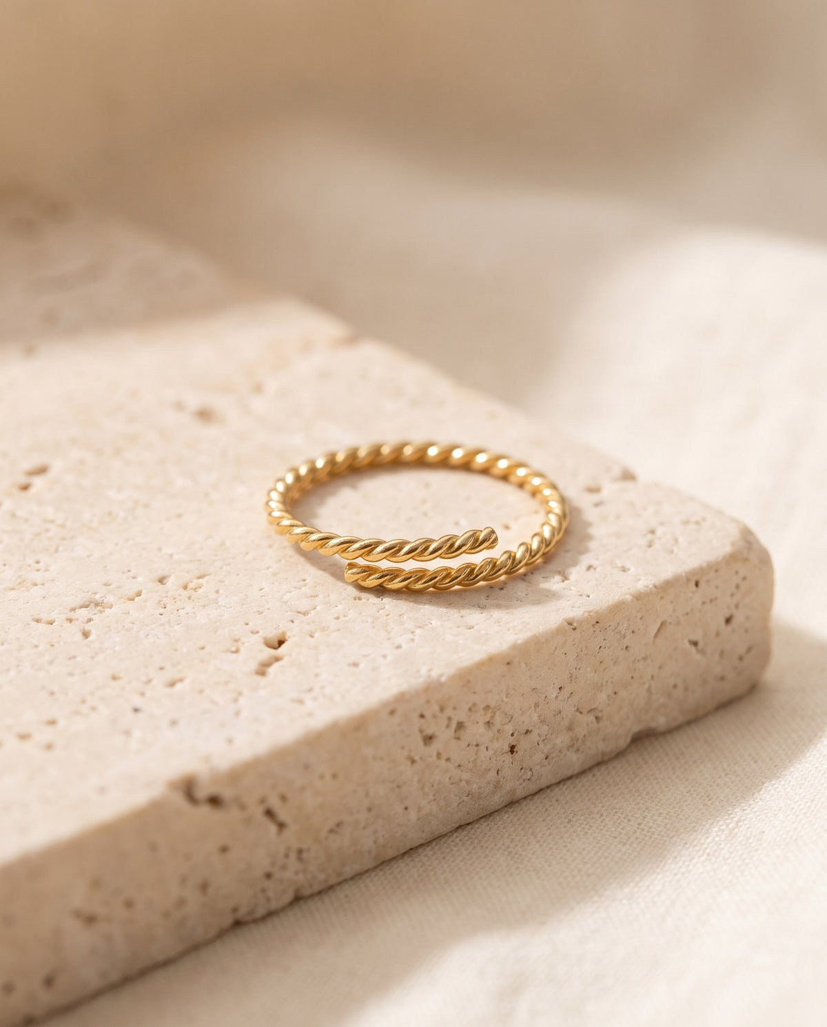 Slim gold-plated Twisted Open Ring with an adjustable open front on a travertine block
